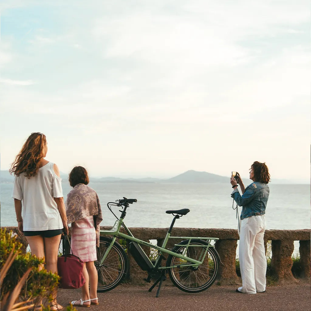 3 femmes de dos et un vélo vert devant la mer à Biarritz