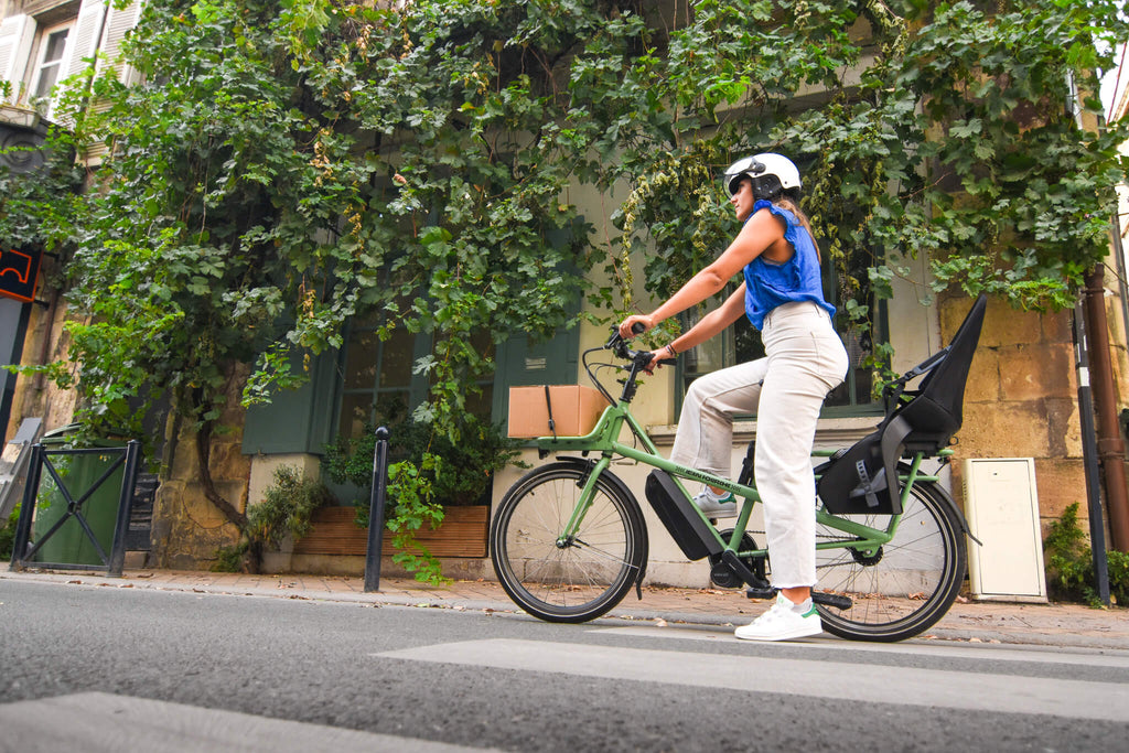 femme en velo cargo electrique vert dans une rue