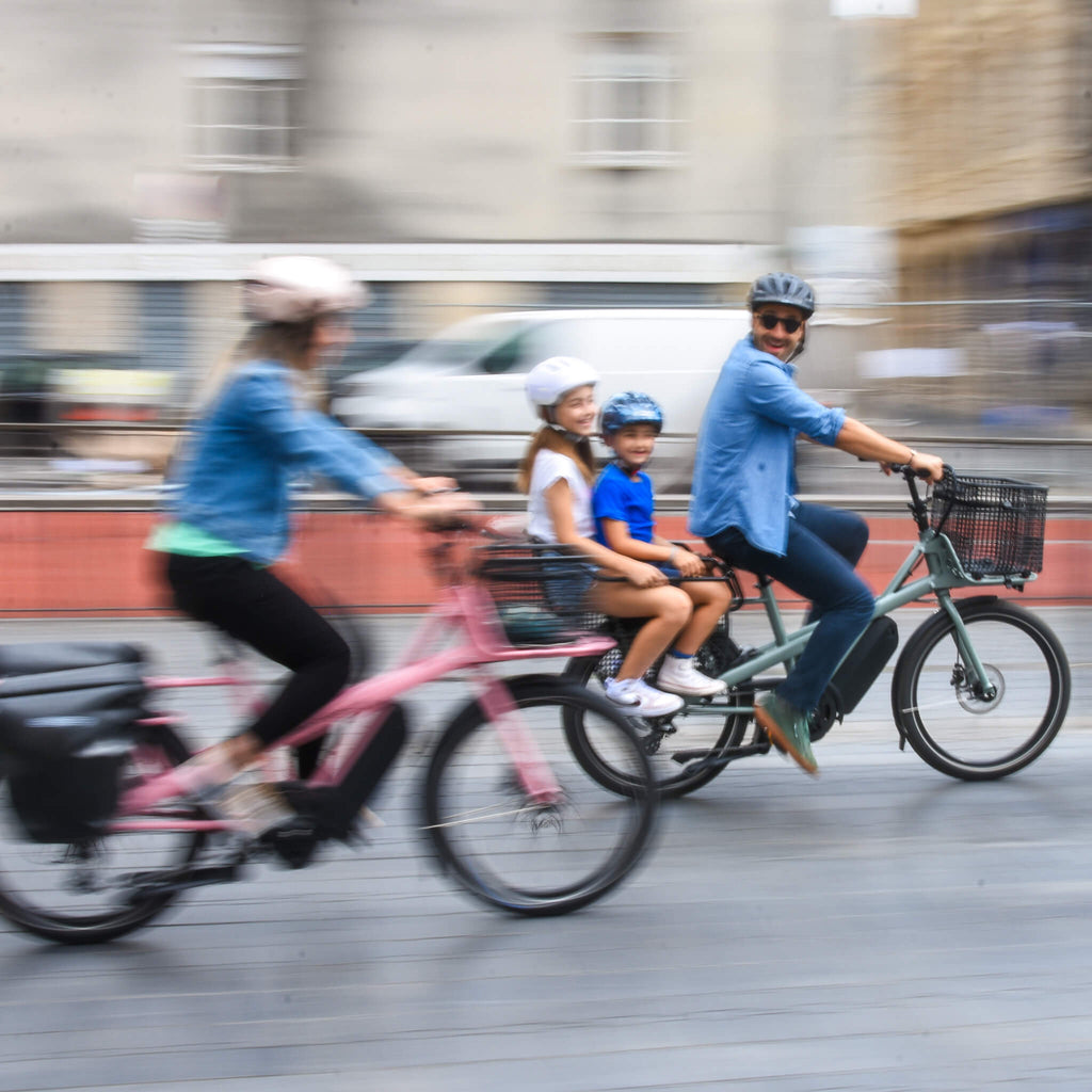 1 famille sur 2 vélos cargo compact, photo floue prise de côté